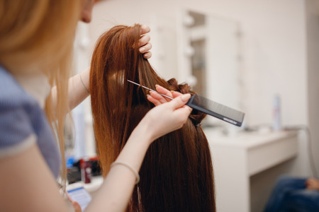 Woman hairdresser making hairstyle to blonde girl in beauty salon.の写真素材