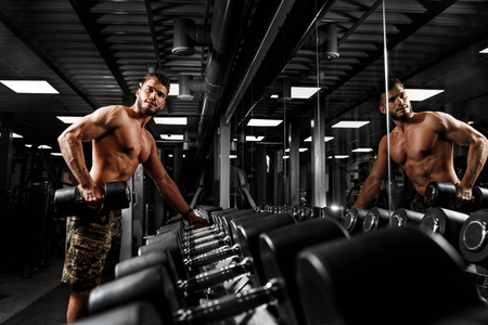 Muscular man with dumbbells in gym opposite mirror.の写真素材