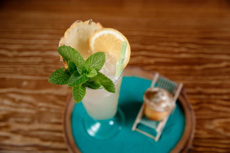 Refreshing cocktail with alcohol, mint, orange and ice in tall glass. Peach is lying on chaise longue on beach.の写真素材