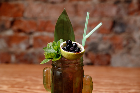 Refreshing alcoholic cocktail with blueberries and lime in glass bottle on brick wall background.の写真素材
