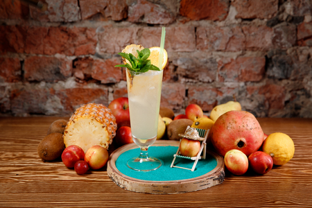 Refreshing cocktail with alcohol, mint, orange and ice in tall glass. Background mix of fruits, Brick wall.の写真素材