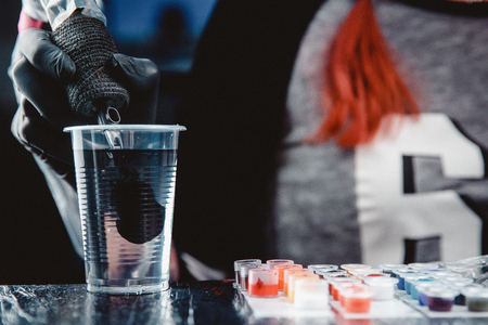 Close-up of tattoo machine is washed with needles in clear water from pigment of paint.の写真素材