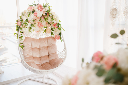 Chair on chains levitates in white room. Decorated with flowersの写真素材