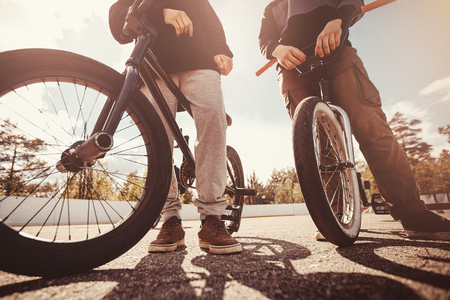 Group of teenage friends are riding bicycles bmx, doing tricks in park. Sunset light. Concept of extreme sports.の写真素材