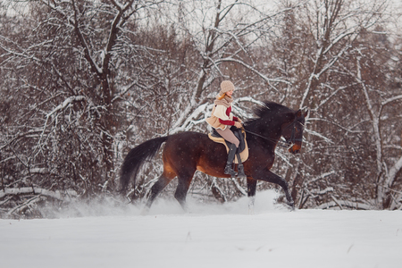 Close-up of girl rider riding gallop on horse through winter forest.の写真素材