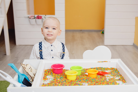 Children boy play at table in colored sand with scoop and bucket, hands in frame. Concept development of motor skills for kid.の写真素材
