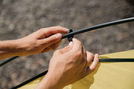 Man hands gather yellow tent, inserts into fastening loops.の写真素材