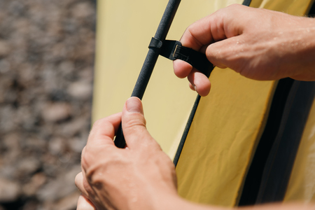 Man hands gather yellow tent, inserts into fastening loops.の写真素材