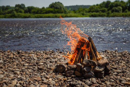 Bonfire is laid out of logs, it edged with stones, in background bank of lake, campingの写真素材
