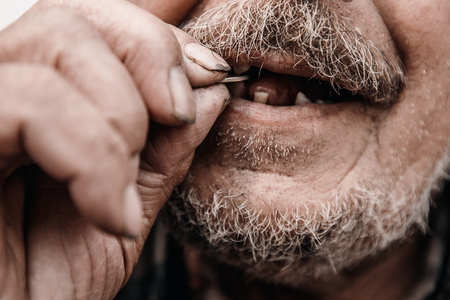 Old man without teeth bites coin capitalism society.の写真素材