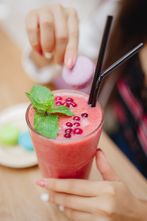 Young woman is holding useful smoothies red from fresh berries and fruits in cafe with French macaroons.の写真素材