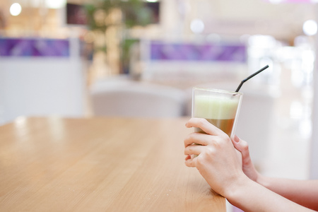 Cold coffee with ice in woman hand, blurred background.の写真素材
