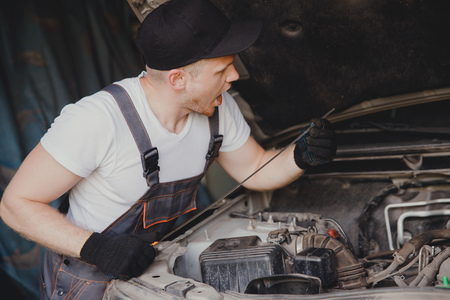 Car mechanic working diagnostic equipment at automotive service. Checking oil level.の写真素材