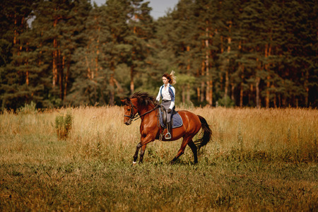 Young woman jockey gallop brown horse strolling across field. Concept rest for rich people.の写真素材