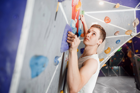 Close-up of male climber on sport climbing gym wall holding onto ledges.の写真素材