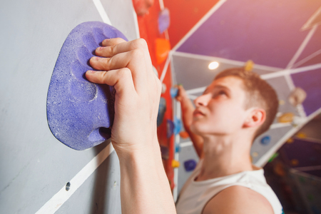 Close-up of male climber on sport climbing gym wall holding onto ledges.の写真素材