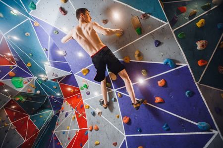 Close-up of male climber on sport climbing gym wall holding onto ledges.の写真素材