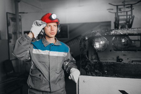 Young miner man underground in mine for coal mining overalls is busy with work, repairing against backdrop of equipment. Portrait.の写真素材