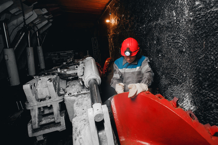 Young miner man underground in mine for coal mining overalls is busy with work, repairing against backdrop of equipment. Portrait.の写真素材