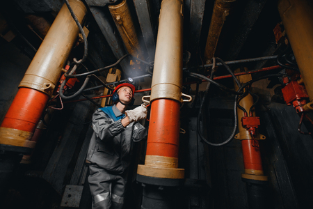 Young miner man underground in mine for coal mining overalls is busy with work, repairing against backdrop of equipment. Portrait.の写真素材