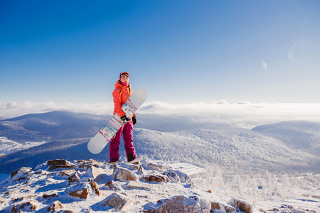 Young woman Standing on top of a mountain and holding a snowboard in hands, goggles.の写真素材