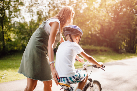 Mom and little boy learning to ride bicycle park having fun togetherの写真素材