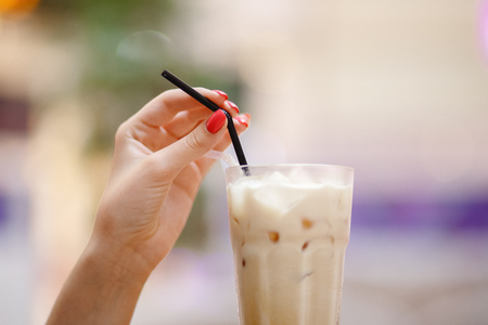 Cold coffee with ice in woman hand, blurred background.の写真素材