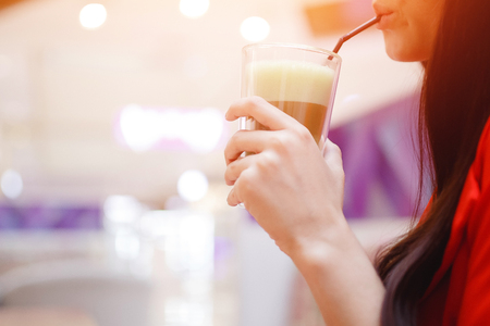 Woman drinks from tubule cold coffee with ice, blurred background.の写真素材