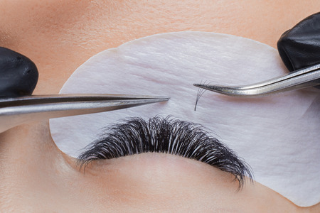 Eyelash extension procedure. Woman master making long lash with tweezersの写真素材