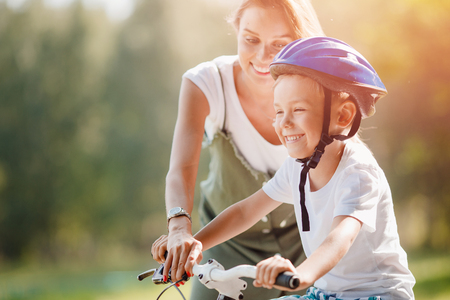 Little boy learns how to ride bicycle, his sister is happy and laughs success. Concept family, support.の写真素材