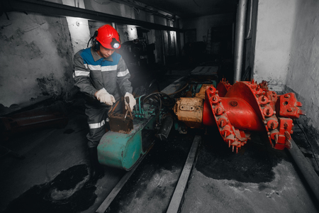 Young miner man underground in mine for coal mining overalls is busy with work, repairing against backdrop of equipment. Portrait.の写真素材