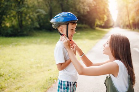 Sister helps younger brother fastens protective helmet for learning to ride bike. Concept family.の写真素材