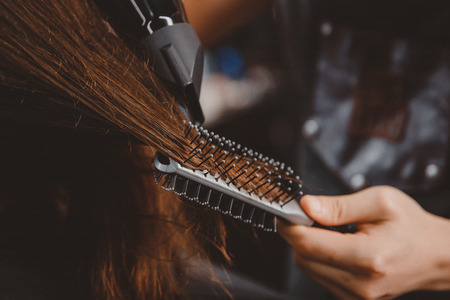 Close-up of drying long hair with hairdryer and combの写真素材
