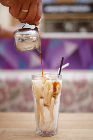 Barista prepares summer cold coffee with ice and milk in transparent glass.の写真素材