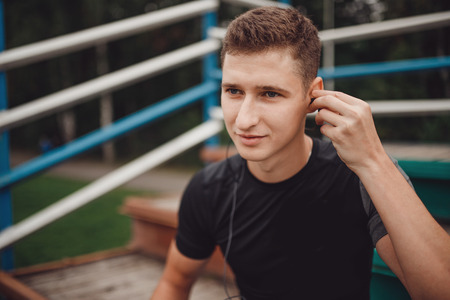 Fitness runner man before training puts on headphones listen music from telephoning. Concept of technology and sport.の写真素材