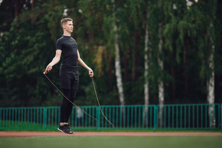 Male athlete performs exercise jump on rope in stadiumの写真素材