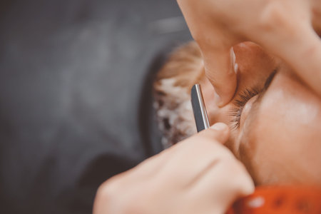 Close-up of barber shearing beard to man in barbershop