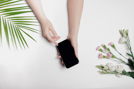 Phone is surrounded by organic natural objects on white background in hands of young beautiful woman.の写真素材