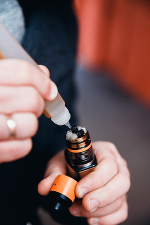 Close-up man is filling an electronic cigarette with a fragrant liquid on a fleece. The spiral is hot. The concept of replacement of cigarettes with tobacco, harmless smoking.の写真素材