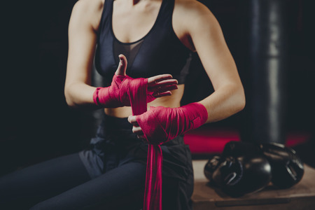 Athletic boxer female wraps bandages on her hands puts gloves for fight in gymの写真素材