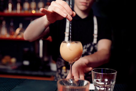 Barman prepares cocktail in transparent glass on bar with alcohol. Dark background.の写真素材