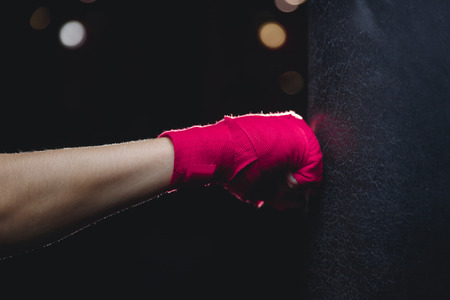 Close-up of hand in fist pink protective insulating bandage hits punching bag on black background. Concept Boxingの写真素材