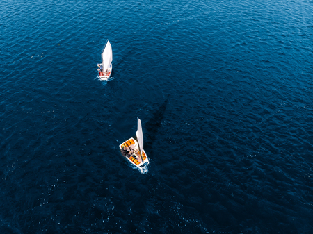 Two white sailing boats cut the deep blue waters river on Sunny autumn day. Top view aerial droneの写真素材