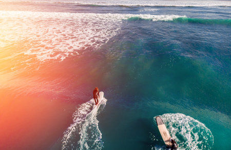 Team of friends in wetsuits surfing on blue water aerial photo