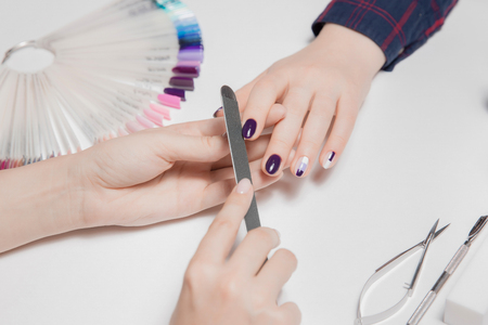 Hands ofwoman. Filing. Final process of creating manicure. Beautiful decorative coating with colored nail Polish. Tools to work in foreground. Palette on backの写真素材