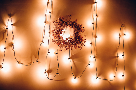 Christmas illumination, wreath decorated with bulbs on thread, against background of wall, warm light.の写真素材