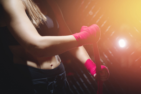 Close-up of hand reels pink protective MMA bandage for fights without rules, blurred background woman sportswoman in short top with pressの写真素材