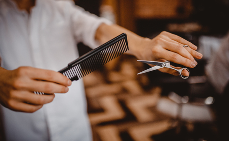 Barber in white shirt holding scissors and comb, at time cutting, background is blurred. Concept of men styleの写真素材