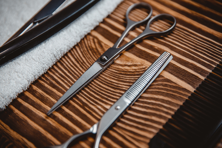 Close-up of metal scissors for men haircuts wooden table, dangerous razor lies on white towel in backgroundの写真素材