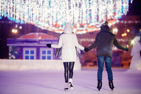 Winter skates, loving couple holding hands and rolling on rink. Illumination in background, night. Concept training. Back view.の写真素材